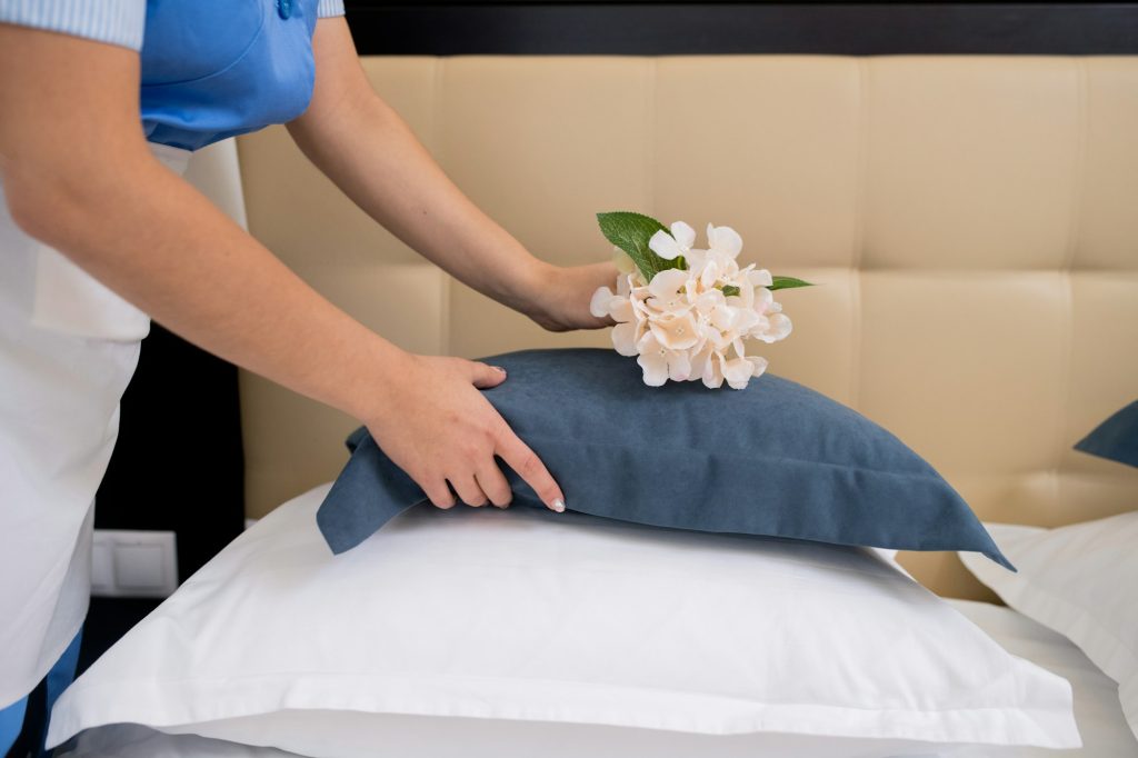 Chamber maid bending over bed while putting fresh flowers on top of pillow